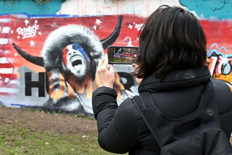A PERSON TAKING A PIC OG A Q-ANON GRAFFITI